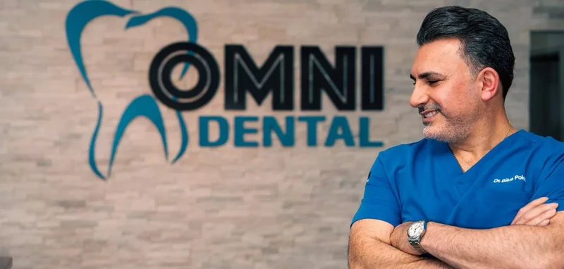 Dr. Bilus Poles in front of the Omni Dental logo wall in Arlington Heights